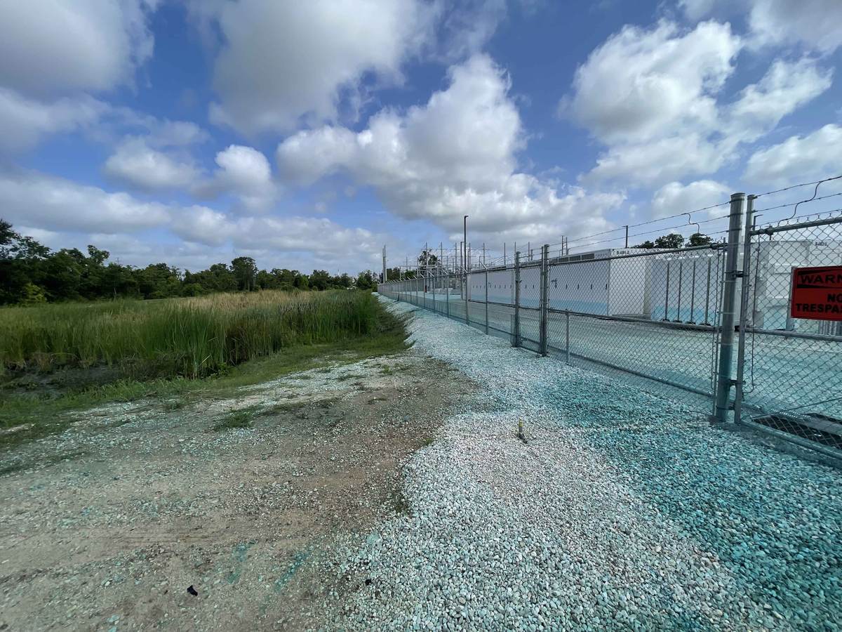 Chain link perimeter fence running along a battery storage yard beside tall grass