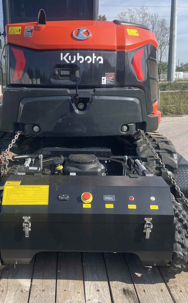 Tracked mower chained down on a trailer behind a mini excavator