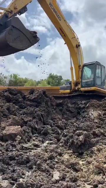 Excavator bucket digging into a large dirt pile